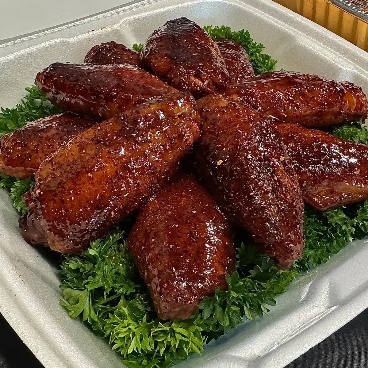 Smoked BBQ chicken wings with a glossy glaze, arranged on parsley in a turn-in box