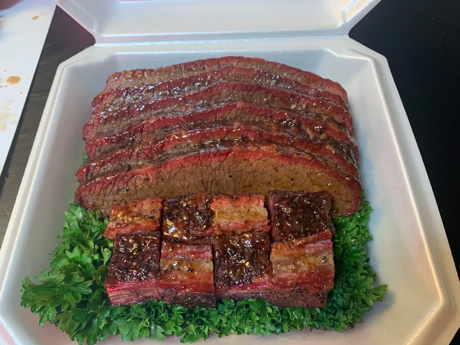 Sliced smoked brisket with cubed burnt ends arranged below on a bed of parsley